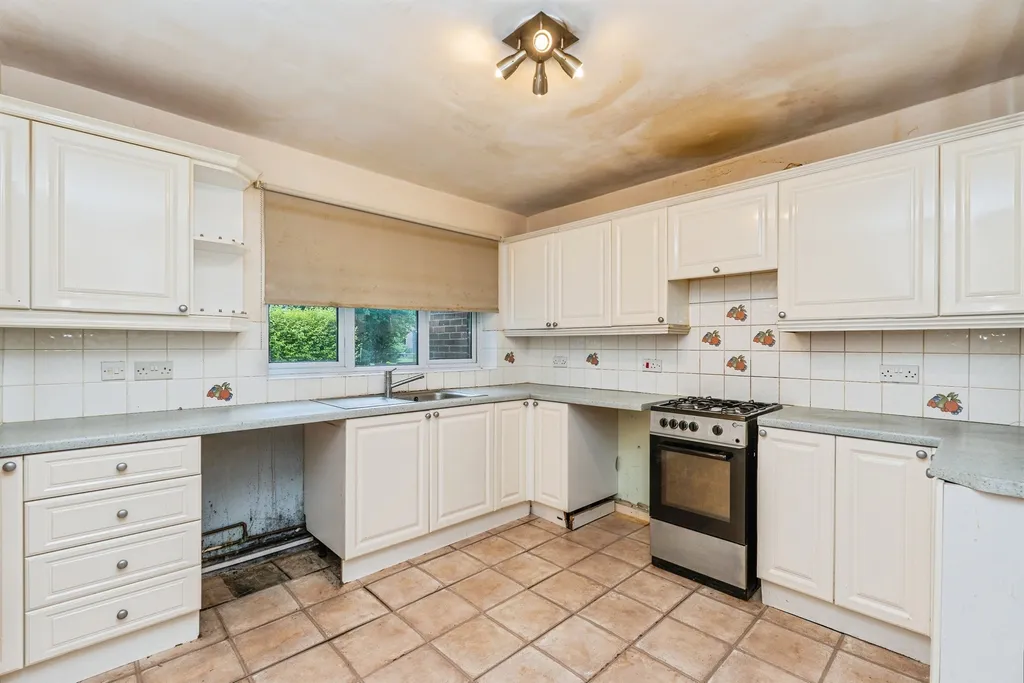 Kitchen with white cabinets, gas oven, tiled floor and walls, and a rear window.