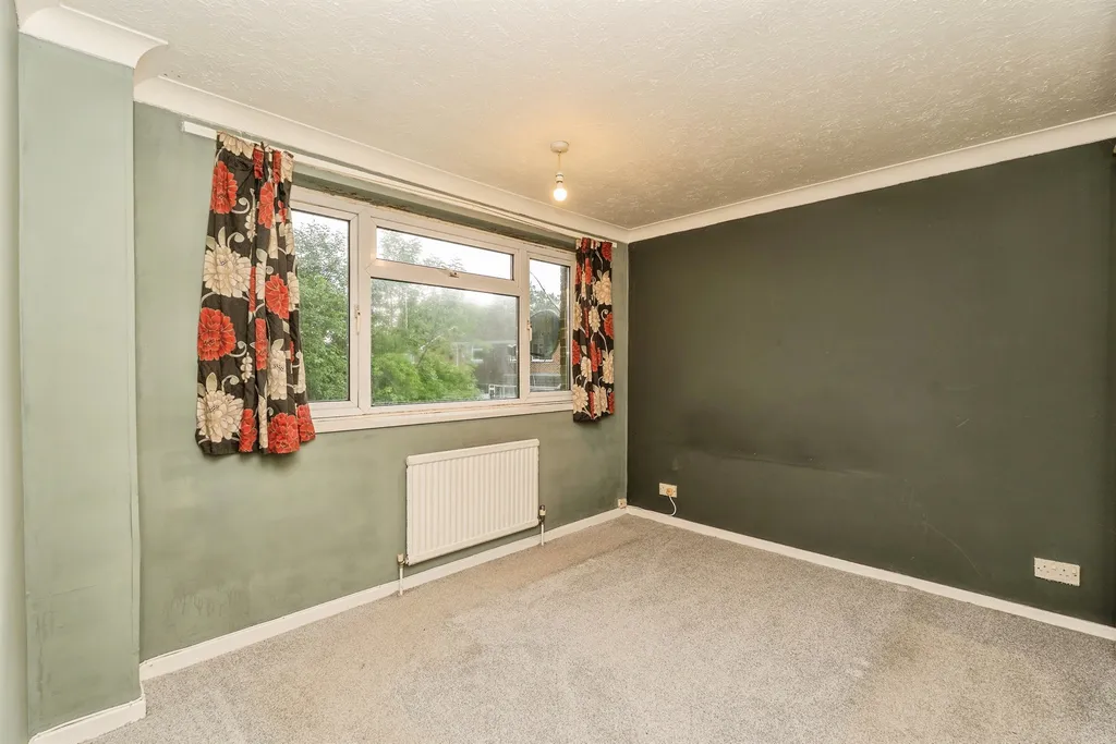 Bright and spacious main bedroom with carpeted floor, radiator, and front-facing window.